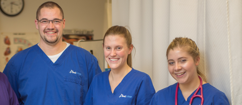 three Beal medical students wearing blue scrubs smiling at the camera