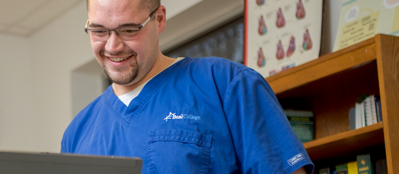 A man wearing blue scrubs smiling at a computer