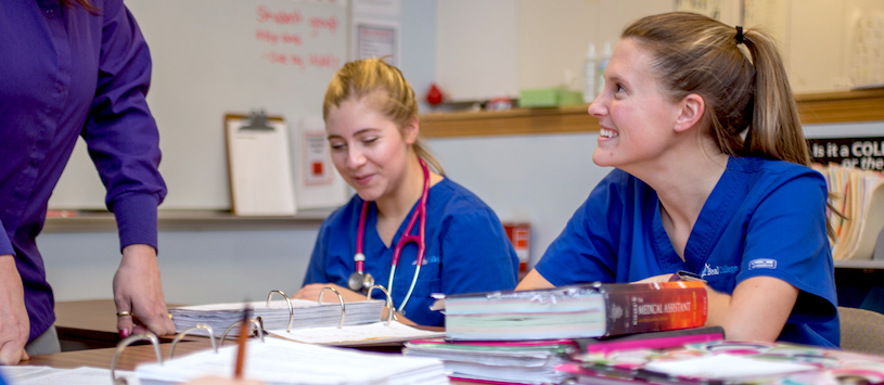 A group of medical students sitting amongst a pile of books laughing. If you want to take a Medical Administrative Specialist Program call Beal.