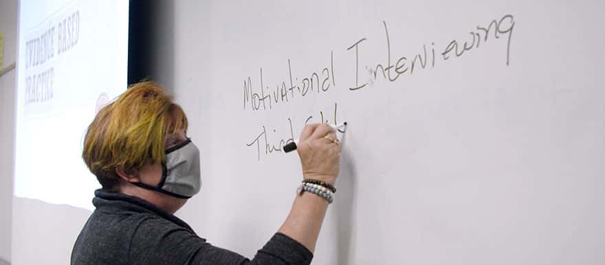Female instructor writing notes on a whiteboard in a classroom.